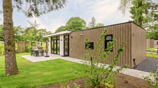 Lodge moderno llamado Module Special Wellness, exterior de madera y terraza rodeada de césped y árboles.