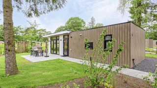 Lodge moderno Module Special Wellness con rivestimento in legno, patio e giardino verde circostante.