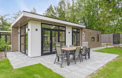 Moderne Lodge mit großer Terrasse und Essmöbeln im Bospark Ede, umgeben von Bäumen in den Niederlanden.
