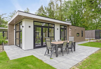 Moderne Lodge mit großer Terrasse und Essmöbeln im Bospark Ede, umgeben von Bäumen in den Niederlanden.