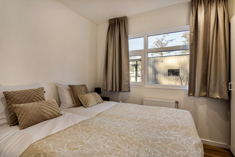 Lichte slaapkamer met tweepersoonsbed, beige gordijnen en kussens in een lodge in Bospark Ede, Nederland.