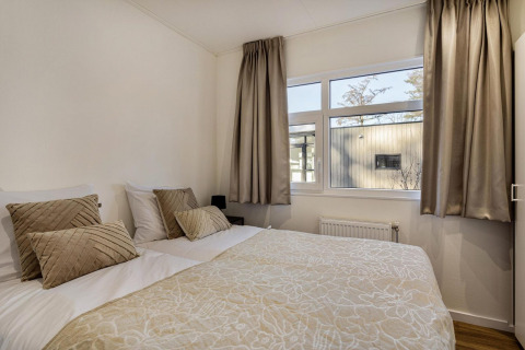 Dormitorio luminoso con cama doble, cortinas y cojines beige en una cabaña en Bospark Ede, Países Bajos.