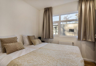 Chambre lumineuse avec lit double, rideaux et coussins beige dans un lodge à Bospark Ede, Pays-Bas.