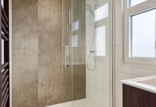 Doccia moderna con porta in vetro e soffione a pioggia in un bagno lodge al Bospark Ede, Paesi Bassi.