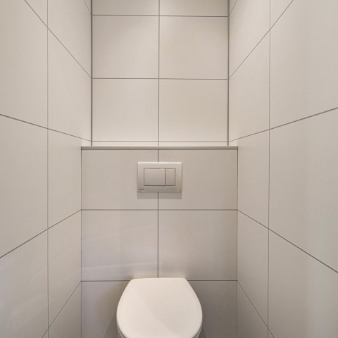 Minimalist bathroom with white tiles and a wall-mounted toilet inside Module Special Wellness at Bospark Ede.