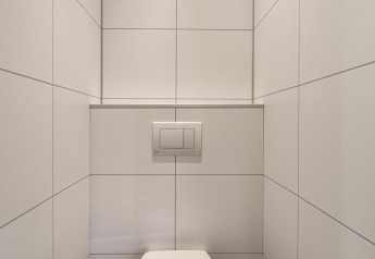 Minimalistisk badeværelse med hvidt flisegulv, væghængt toilet og skjult cisterne på Bospark Ede-lodgen.