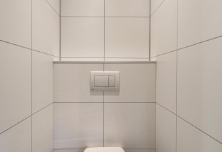 Modernes Badezimmer mit weißen Fliesen, wandhängendem WC und Spülkasten im Bospark Ede Lodge, Niederlande.