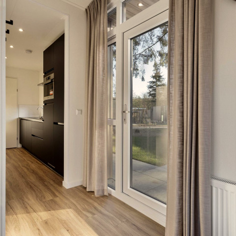 Moderne lodge bij Bospark Ede, Nederland met grote ramen, keuken en beige gordijnen, houten vloer.