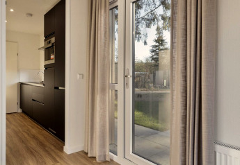 Moderne lodge bij Bospark Ede, Nederland met grote ramen, keuken en beige gordijnen, houten vloer.
