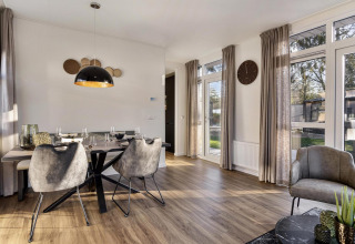 Modern dining and lounge area with large windows in a lodge at Bospark Ede, Netherlands, featuring stylish decor.