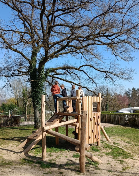 Niños juegan en una estructura de madera bajo un árbol grande en Camping Le Roptai, Namur, Bélgica.