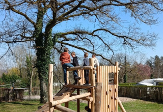 Kinder spielen auf einem Holzspielplatz unter einem Baum im Camping Le Roptai, Namur, Belgien.