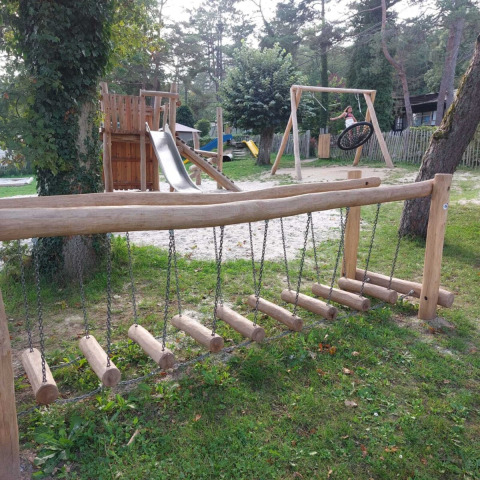 Playground with wooden climbing equipment, slide and swings at Camping Le Roptai, Namur, Belgium, in a forest.