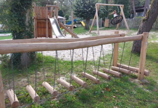 Parco giochi con strutture in legno, scivolo e altalene al Camping Le Roptai, Namur, Belgio, immerso nel verde.