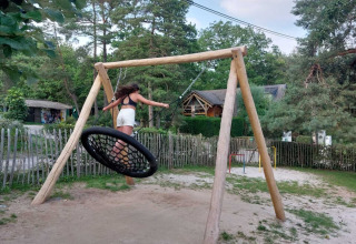 Fille sur une balançoire panier au terrain de jeu, entourée d’arbres à Camping Le Roptai, Namur, Belgique.