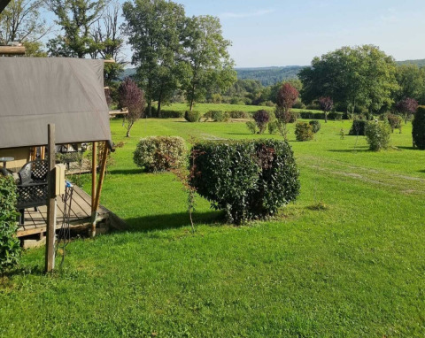 Et fredeligt grønt område på Camping Le Roptai i Namur, Belgien, med buske, træer og en teltstruktur.