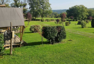 Groene graszone met struiken, bomen en een tentstructuur op Camping Le Roptai in Namen, België.