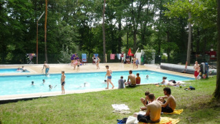 Campistas disfrutando de la piscina rodeada de árboles en Camping Le Roptai, Namur, Bélgica.