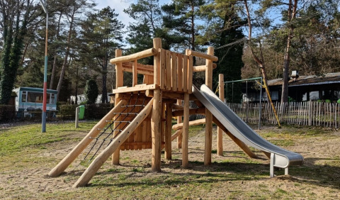 Estructura de juegos de madera con tobogán en Camping Le Roptai en Namur, Bélgica, rodeada de árboles.