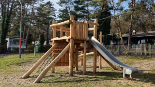 Estructura de juegos de madera con tobogán en Camping Le Roptai en Namur, Bélgica, rodeada de árboles.