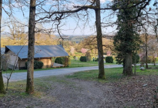Zicht op Camping Le Roptai in Namen, België, met bomen, een hut en een schilderachtig lentelandschap.