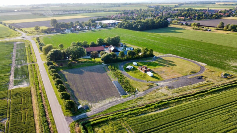 Vista aérea de Minicamping Hofstede Zonnevliet en Zeeland, Países Bajos, rodeado de campos verdes y casas.