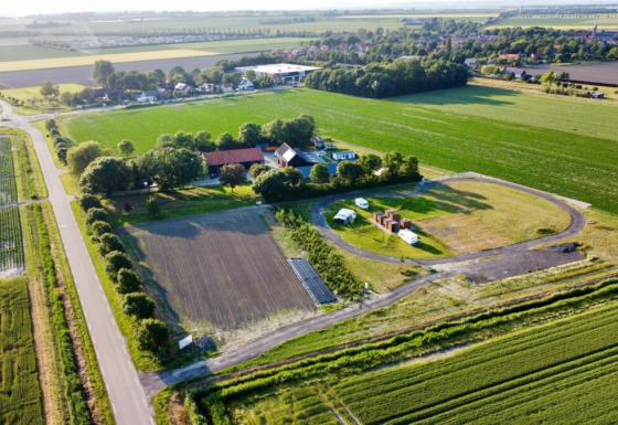 Luchtfoto van Minicamping Hofstede Zonnevliet in Zeeland, Nederland, omgeven door groene akkers en gebouwen.