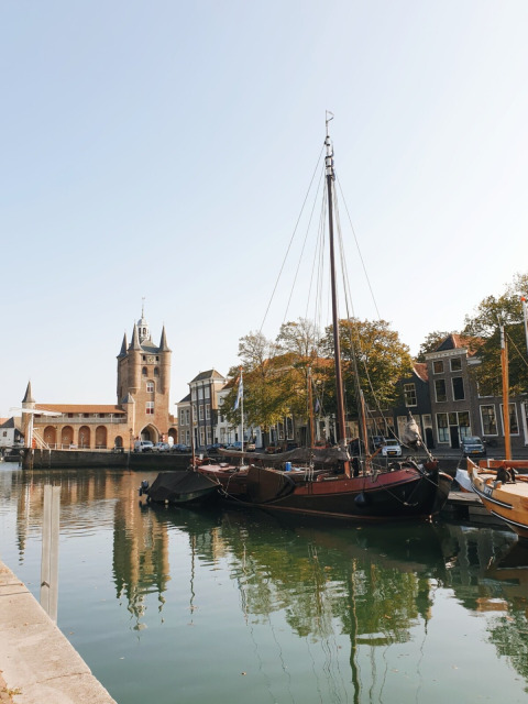 Barcos amarrados junto a un canal soleado, edificios históricos y una torre de reloj en Zeeland, Países Bajos.