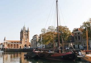 Bootjes aangemeerd aan een zonovergoten gracht met historische gevels en toren in Zeeland, Nederland.