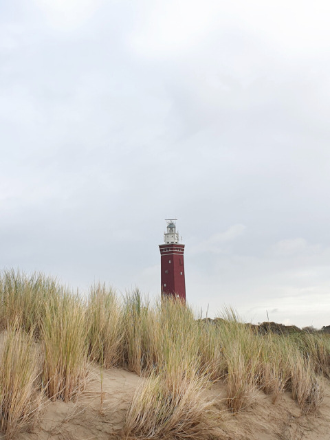 Un faro rojo se alza tras dunas arenosas en Minicamping Hofstede Zonnevliet en Zeeland, Países Bajos.
