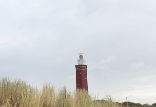 Een rode vuurtoren steekt achter de duinen bij Minicamping Hofstede Zonnevliet in Zeeland, Nederland uit.