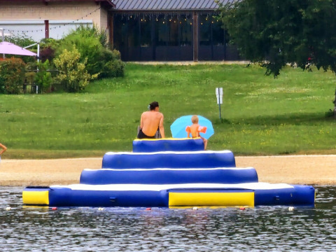 Twee personen zitten op een blauwe opblaasbare structuur bij Camping Montard in Nouvelle-Aquitaine, Frankrijk.