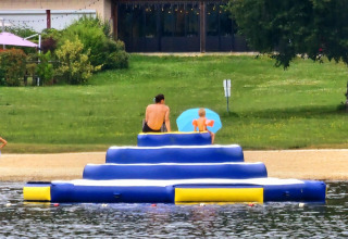 Deux personnes assises sur une plateforme gonflable bleue au bord de l’eau à Camping Montard en Nouvelle-Aquitaine.