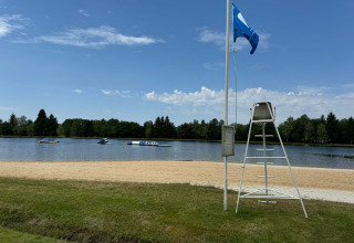 Spiaggia sabbiosa con sedia da bagnino e vista lago al Camping Montard, Nouvelle-Aquitaine, Francia.