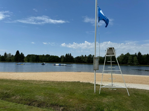 Spiaggia sabbiosa con sedia da bagnino e vista lago al Camping Montard, Nouvelle-Aquitaine, Francia.