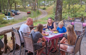 Familie nyder et måltid ved et bord udendørs på Camping Montard i Nouvelle-Aquitaine, Frankrig.