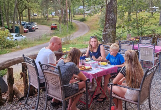 Familie nyder et måltid ved et bord udendørs på Camping Montard i Nouvelle-Aquitaine, Frankrig.