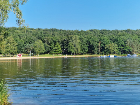 Vista del lago y playa en Camping Montard, parque vacacional en Nouvelle-Aquitaine, Francia, con bosque al fondo.