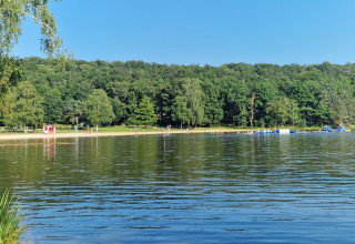 Vista del lago y playa en Camping Montard, parque vacacional en Nouvelle-Aquitaine, Francia, con bosque al fondo.