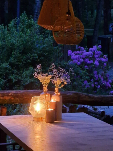 Mesa exterior con velas y flores en Camping Montard, rodeada de vegetación y flores moradas.