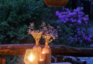Ein Tisch mit Kerzen und Blumen im Freien im Camping Montard, umgeben von grünen Büschen und lila Blumen.