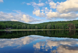 Lake view at Camping Montard in Nouvelle-Aquitaine, France, with lush trees and cloud reflections on the water.