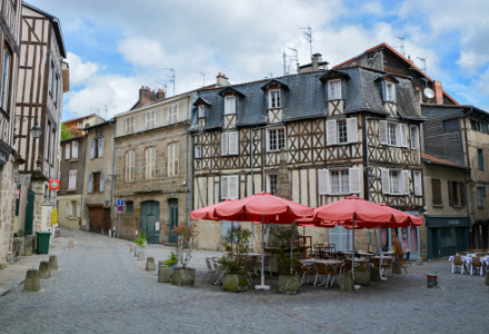 Encantadora plaza cerca de Lamongerie, Nouvelle-Aquitaine, con casas entramadas y sombrillas rojas de café.