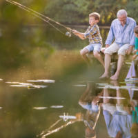 Un hombre mayor y dos niños pescan y juegan con un barco de juguete sobre un muelle en Lamongerie, Francia.