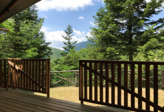 View from a wooden deck overlooking lush trees and hills at Camping Il Collaccio in Umbria, Italy.