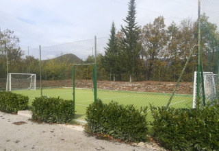 Outdoor football field with goals and fencing, surrounded by trees, at Camping Il Collaccio in Umbria, Italy.