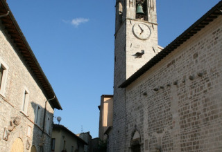 Photo of a bell tower and old stone houses along a narrow street in Umbria, Italy, under a clear blue sky.