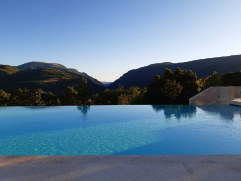 Piscina infinita con vistas a las montañas en Camping Il Collaccio, parque vacacional en Umbría, Italia, al atardecer.