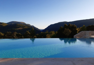 Piscina infinita con vistas a las montañas en Camping Il Collaccio, parque vacacional en Umbría, Italia, al atardecer.