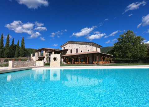 Vista de la piscina y villa de piedra en Camping Il Collaccio, parque de vacaciones en Umbría, Italia.